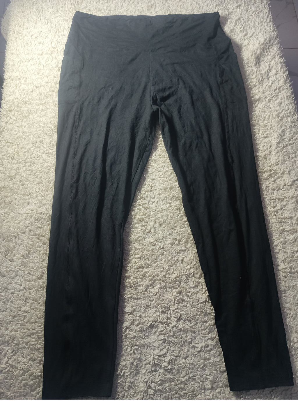 Black leggings laid flat on a textured gray carpet, photographed from above.