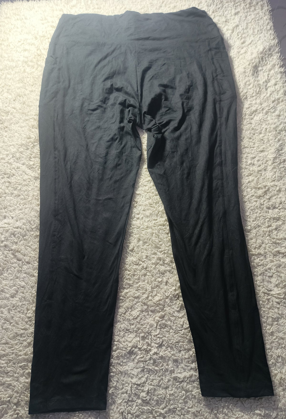 Black high-waisted leggings laid flat on a white shag rug, with a visible crease down the center front.