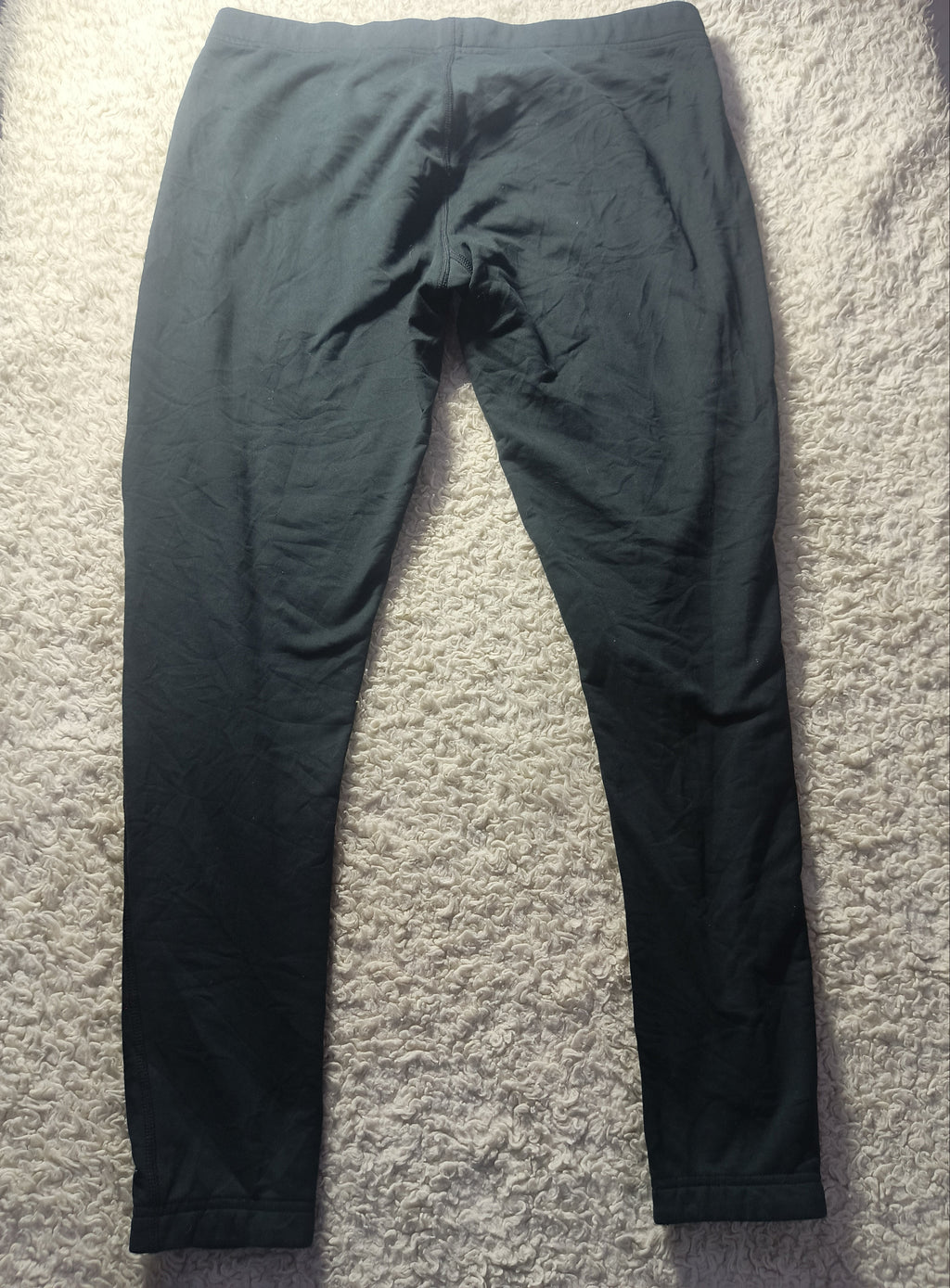 Black athletic pants laid flat on a textured white carpet, with a POVA 6 Neo camera watermark at the bottom.