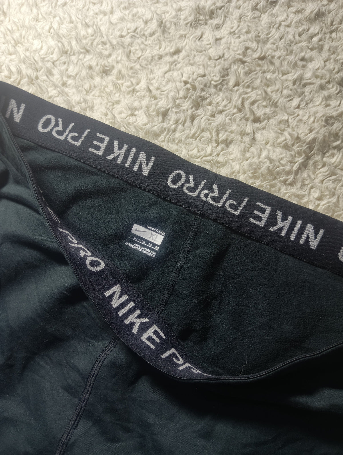 Close-up of a black Nike Pro boxer brief waistband with white lettering, laid flat on a textured beige carpet.