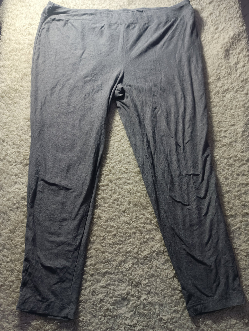 A pair of dark gray lounge pants or sweatpants laid flat on a textured beige carpet. The photo is taken from above with visible wrinkles in the fabric.