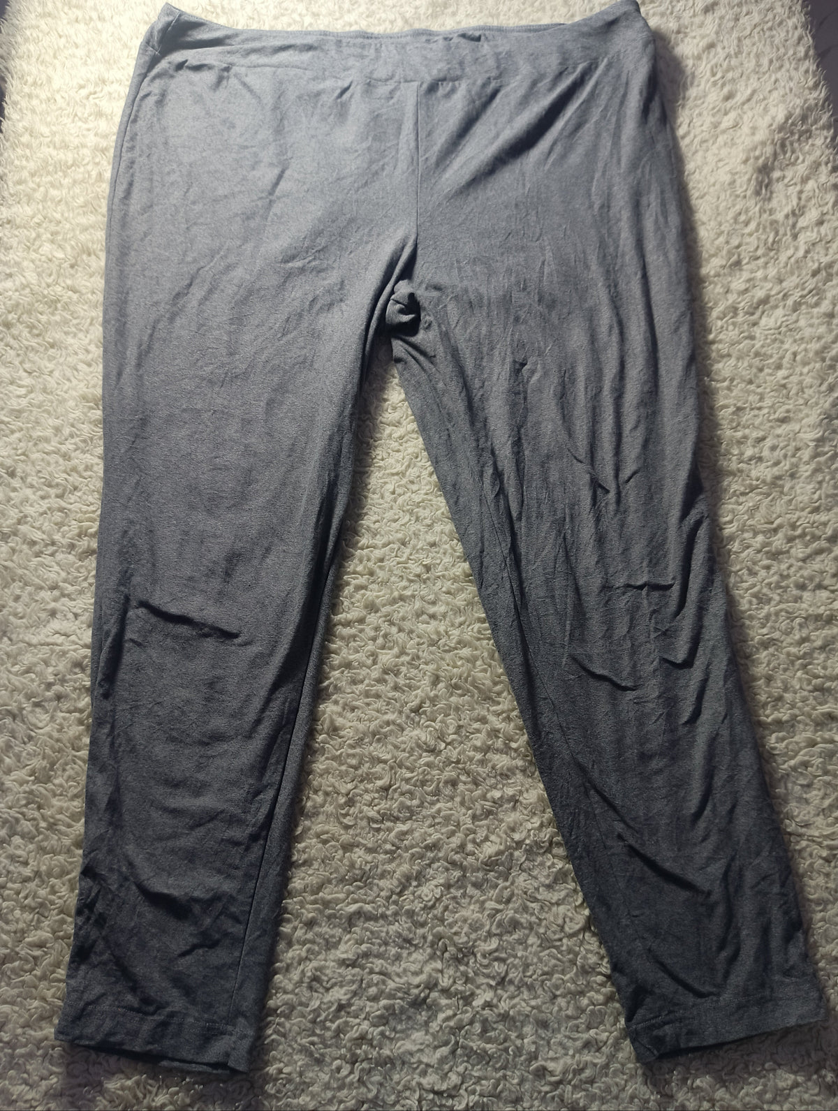 A pair of dark gray lounge pants or sweatpants laid flat on a textured beige carpet. The photo is taken from above with visible wrinkles in the fabric.
