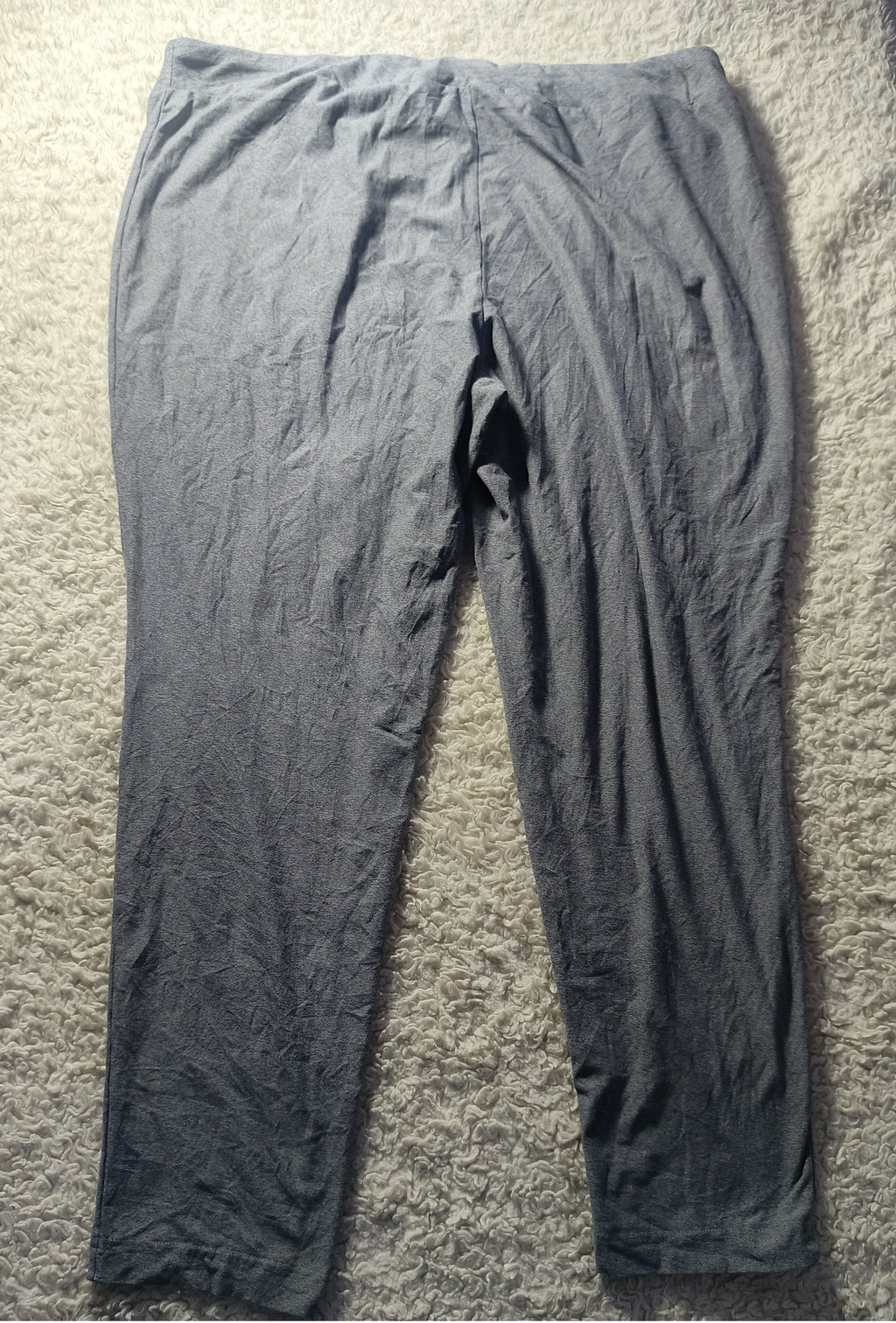 A pair of dark gray crinkled leggings or tights laid flat on a beige carpet. The photo has a camera watermark at the bottom.