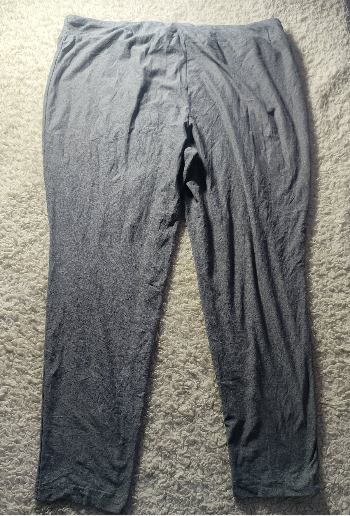 A pair of dark gray crinkled leggings or tights laid flat on a beige carpet. The photo has a camera watermark at the bottom.