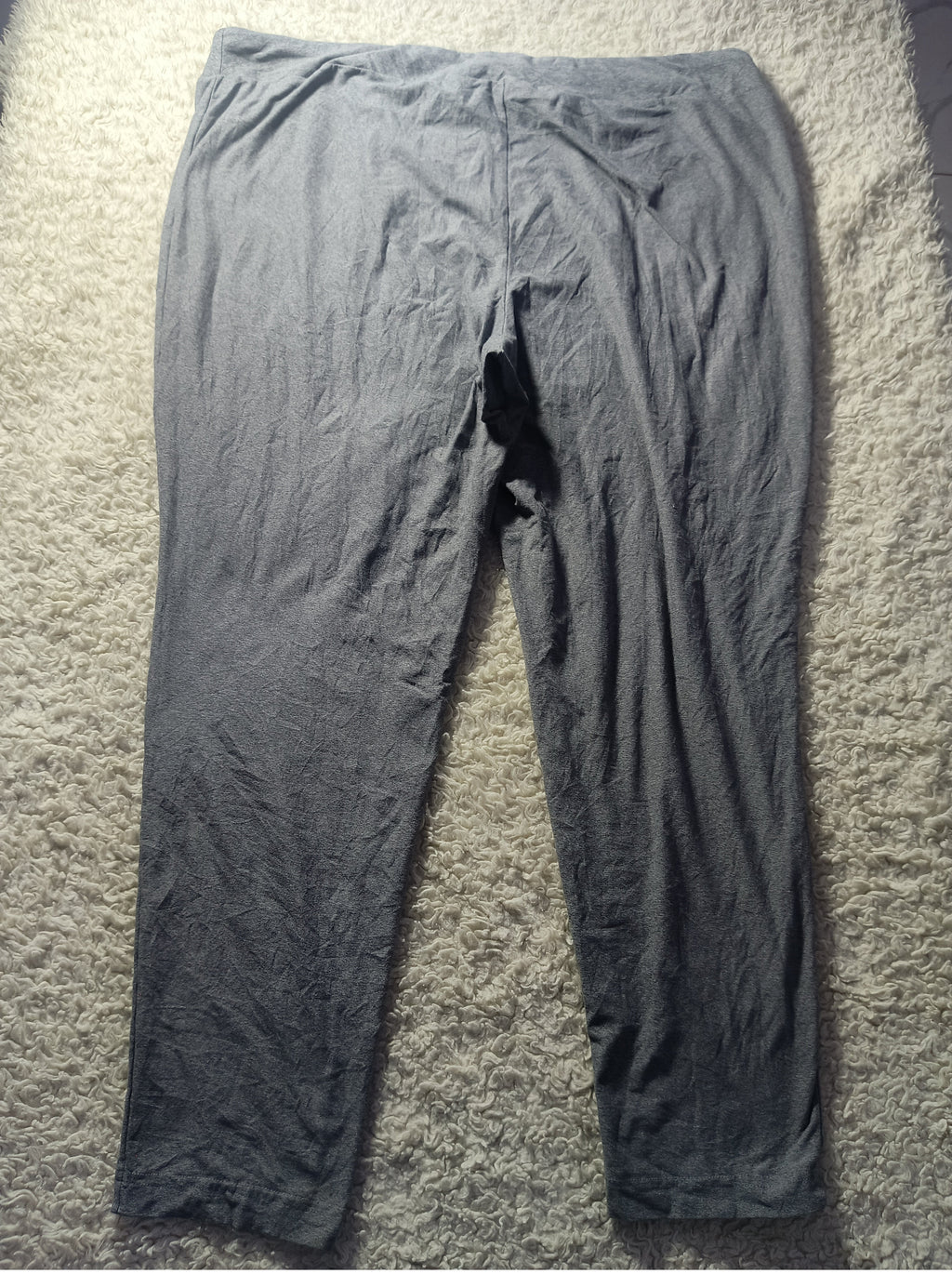 A pair of dark gray crinkled cotton pajama pants laid flat on a textured beige carpet.