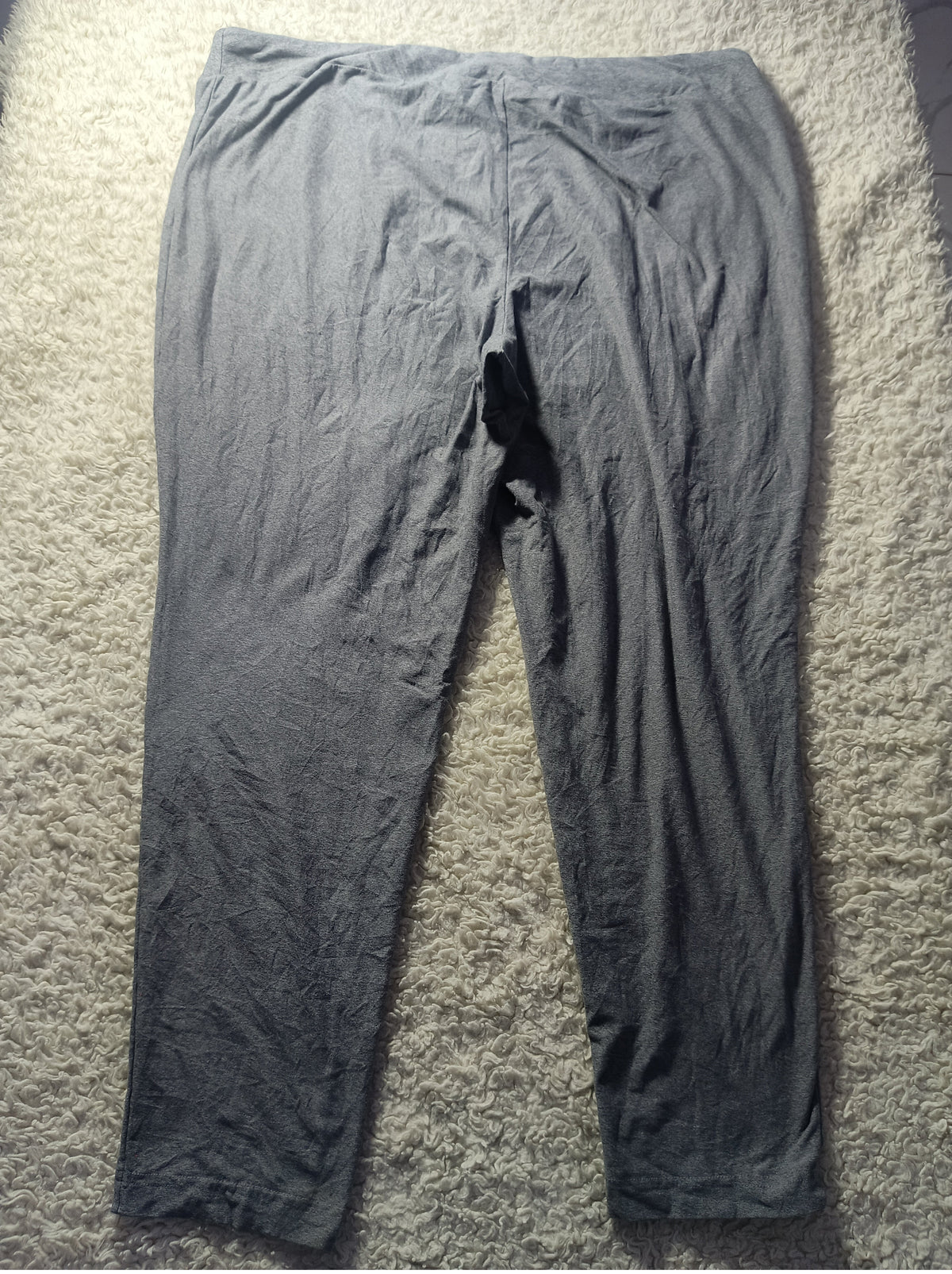 A pair of dark gray crinkled cotton pajama pants laid flat on a textured beige carpet.