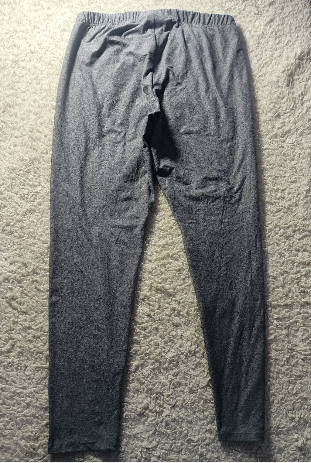 A pair of dark gray heathered lounge pants laid flat on a textured beige carpet, showing the back view with an elastic waistband.
