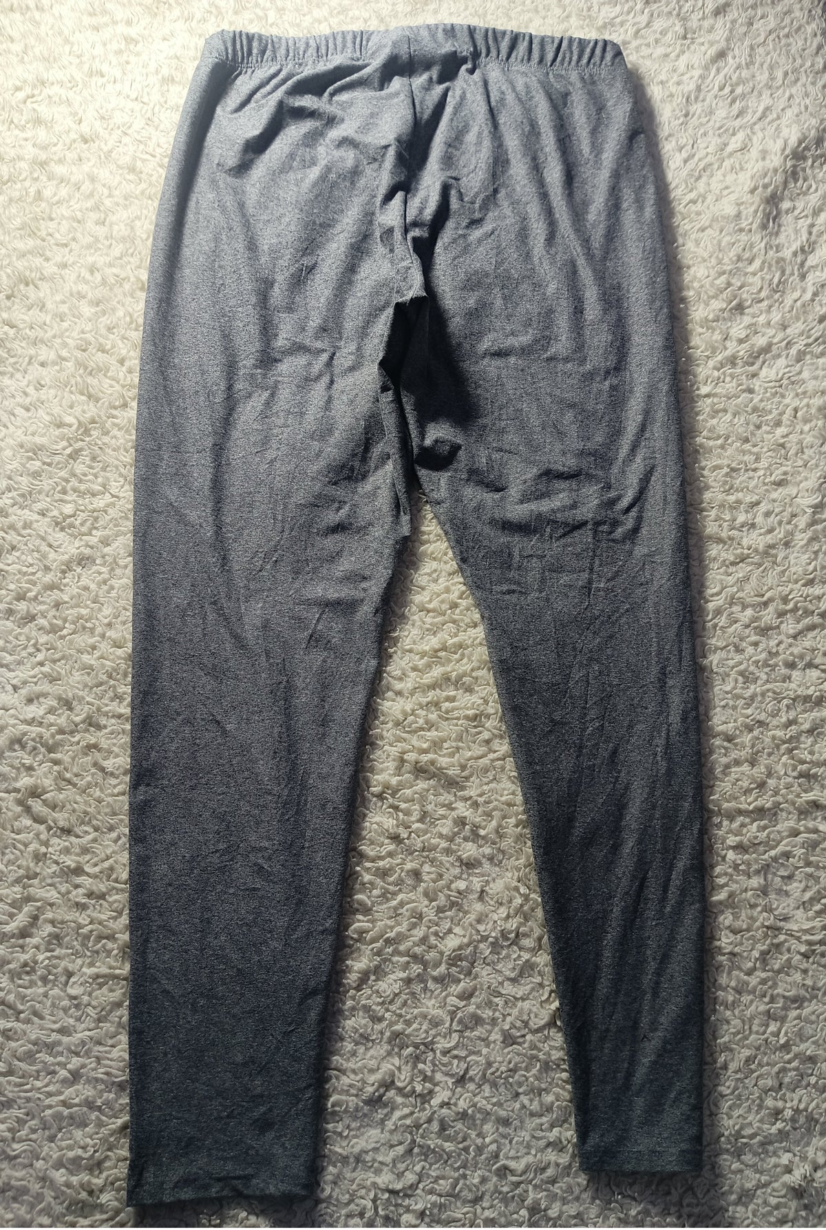 A pair of dark gray heathered lounge pants laid flat on a textured beige carpet, showing the back view with an elastic waistband.
