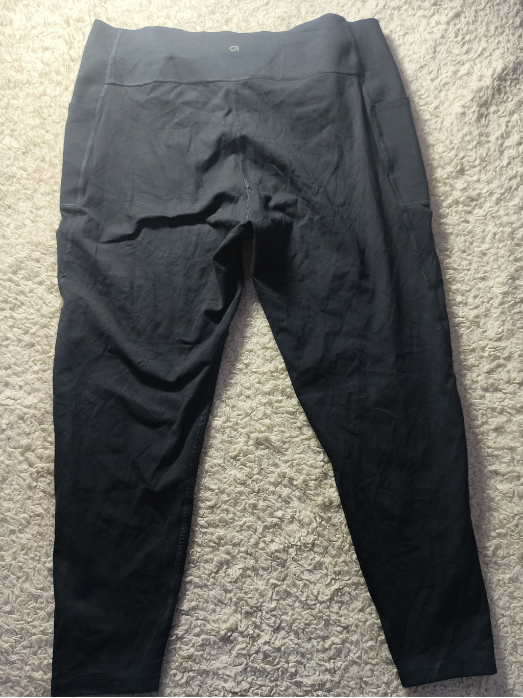 Black athletic leggings laid flat on a textured gray carpet, with a visible waistband and tapered legs.