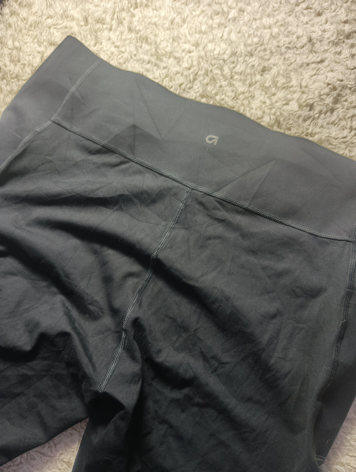 Close-up of dark gray athletic shorts laid flat on a textured beige carpet, showing the waistband, stitching, and leg fabric.