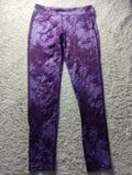 Purple patterned athletic leggings laid flat on a textured gray surface, featuring a diagonal stripe design with a mottled purple and white color scheme.