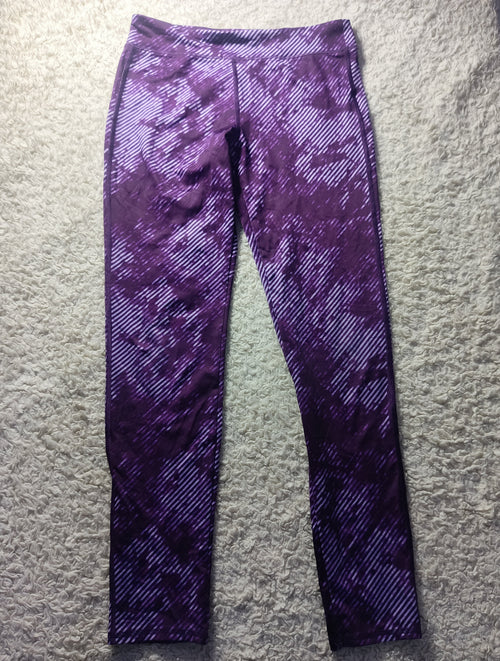 Purple patterned athletic leggings laid flat on a textured gray surface, featuring a diagonal stripe design with a mottled purple and white color scheme.