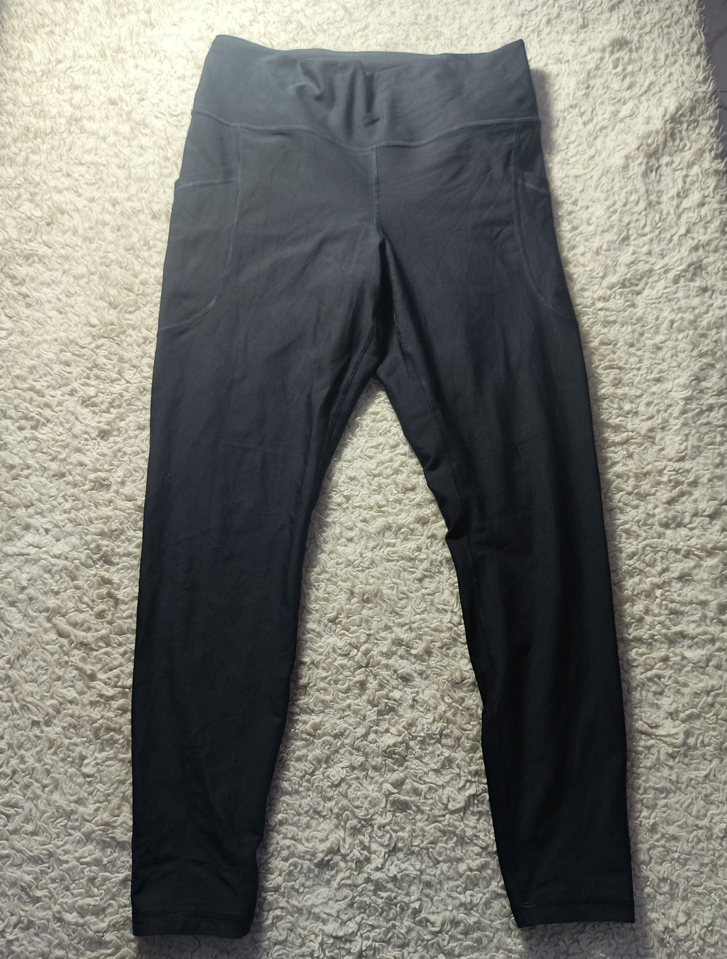 Black high-waisted leggings laid flat on a textured gray carpet, with a camera settings overlay at the bottom.
