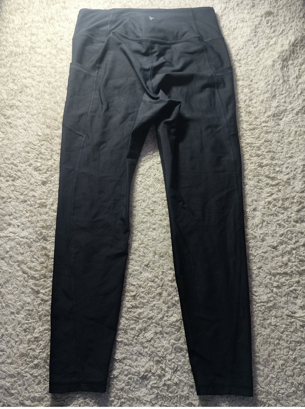 Black high-waisted athletic leggings laid flat on a textured gray carpet background.