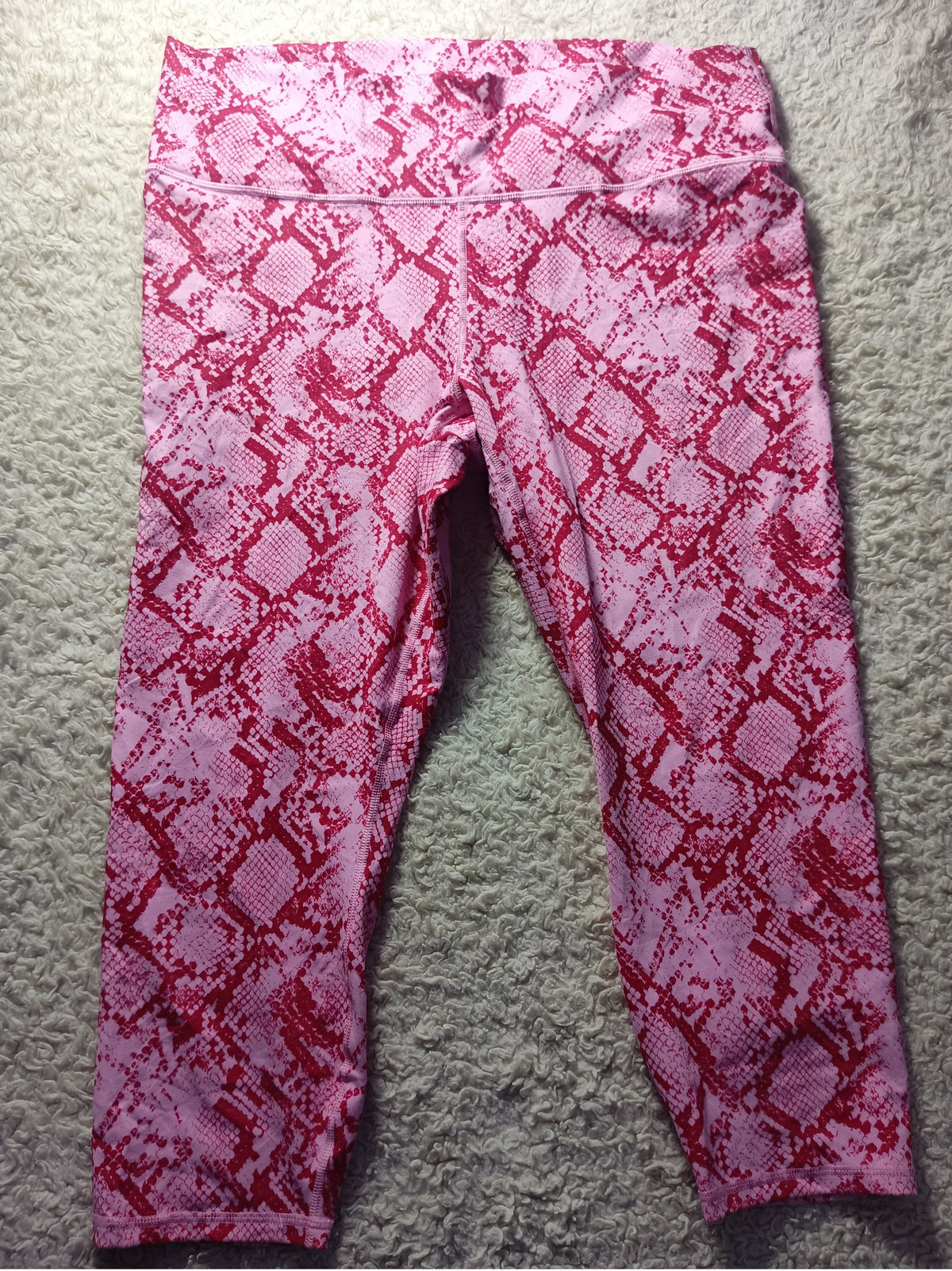 Pink and red snakeskin print leggings laid flat on a gray carpet background.