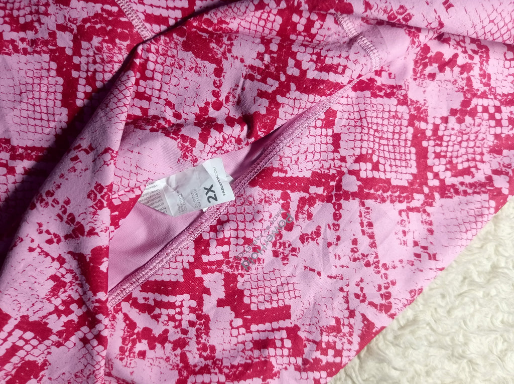 A close-up of a pink and red snakeskin-patterned fabric garment, showing a white size tag marked 'X2'.
