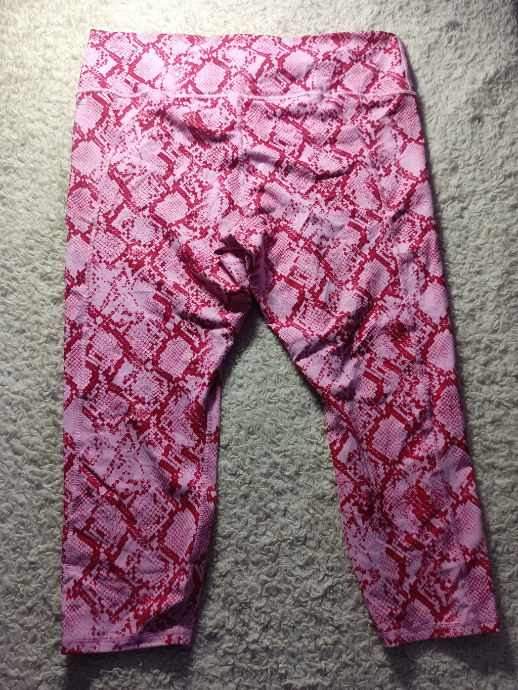 Pink and red snakeskin print leggings laid flat on a gray carpet background.