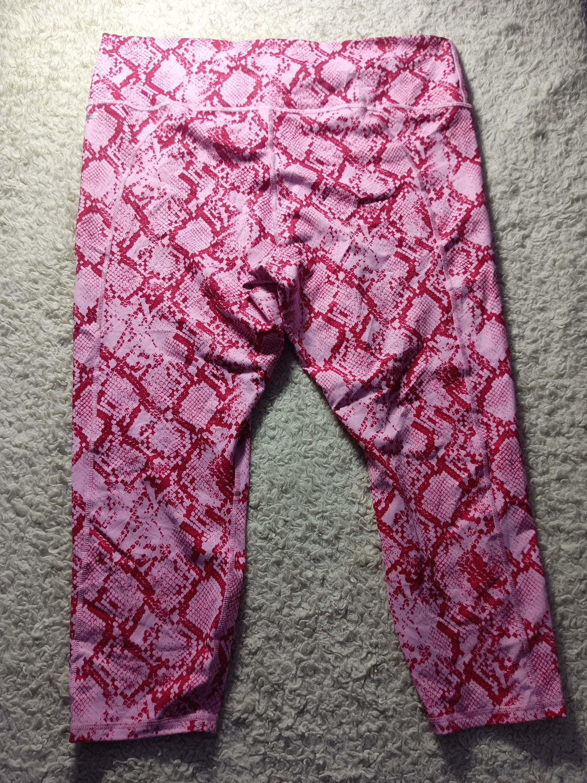 Pink and red snakeskin print leggings laid flat on a gray carpet background.