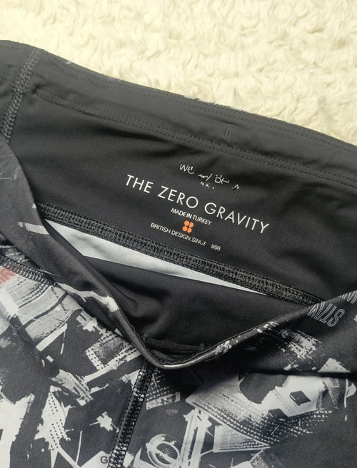 Close-up of a black athletic garment showing the inner neck label with 'THE ZERO GRAVITY' branding, alongside a black-and-white abstract print on the fabric, photographed on a textured cream surface.