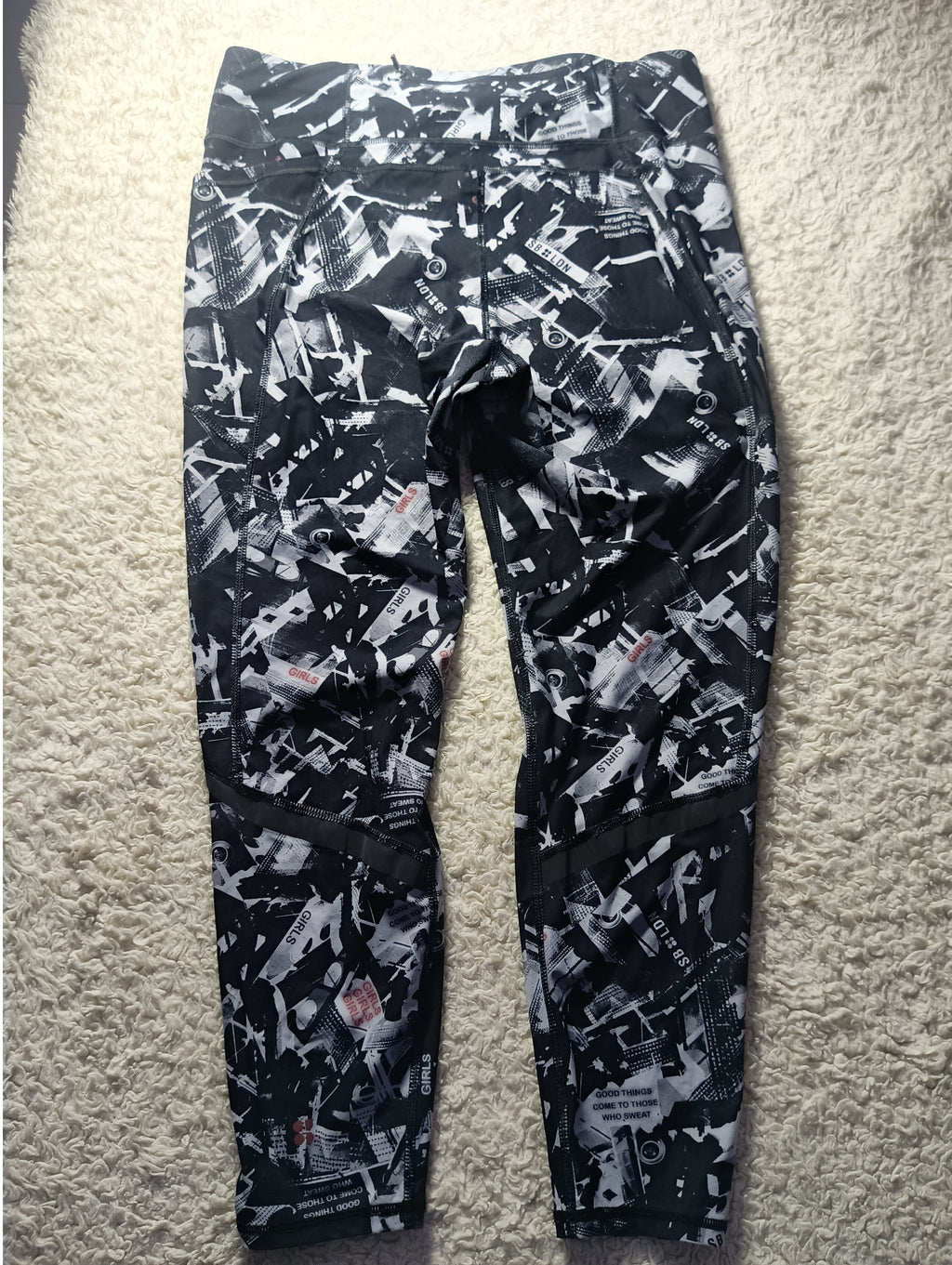 Black and white abstract patterned pants laid flat on a beige carpet background.