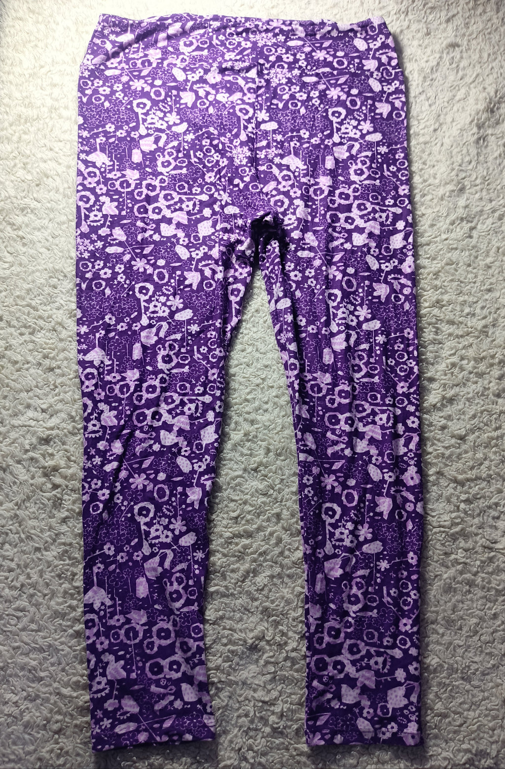 Purple and white patterned leggings laid flat on a white shag rug, with a black drawstring waistband.