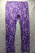 Purple and white patterned leggings laid flat on a white shag rug, with a black drawstring waistband.