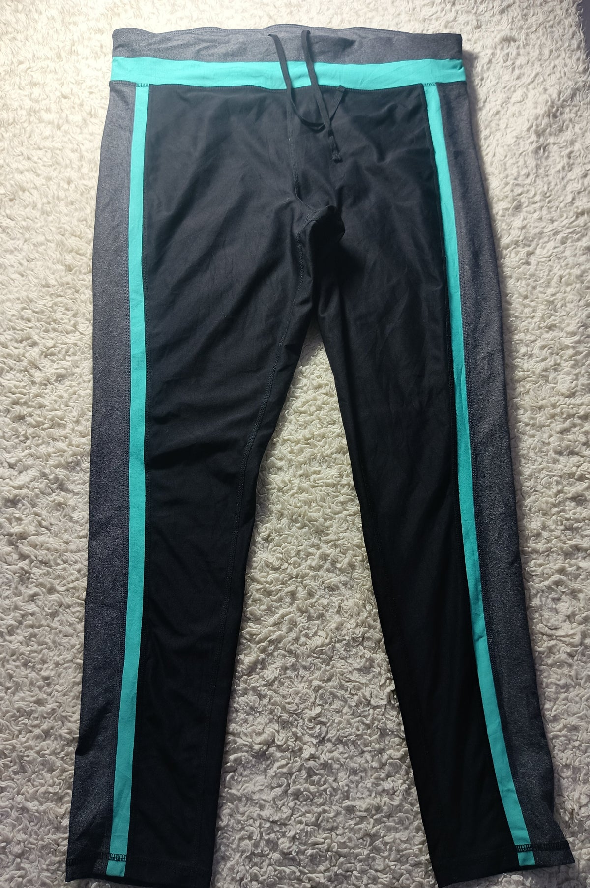 Black athletic leggings with bright teal side stripes and a matching waistband, laid flat on a textured gray carpet.