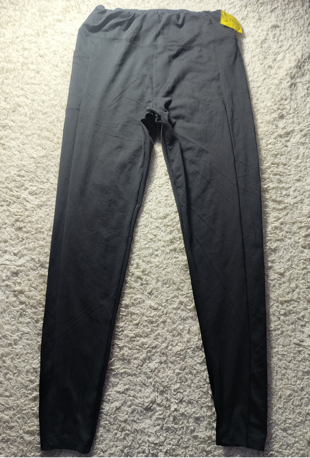 Black high-waisted leggings laid flat on a textured gray carpet, with a small yellow tag visible at the waistband.