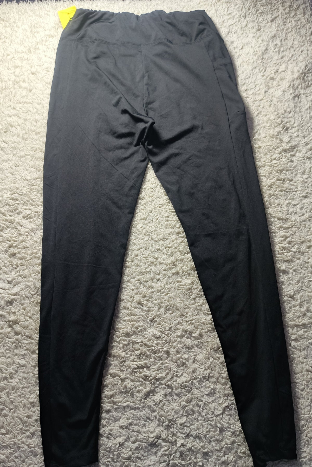 Black athletic leggings laid flat on a textured white shag rug, with a small yellow tag visible at the waistband.