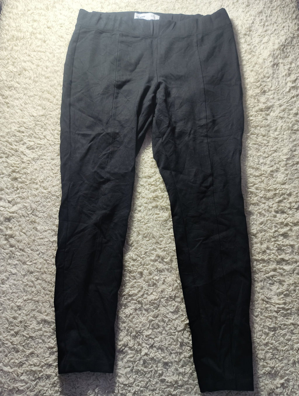 A pair of black wide-leg cropped pants laid flat on a textured beige carpet. The photo is taken from above, with a camera watermark at the bottom.
