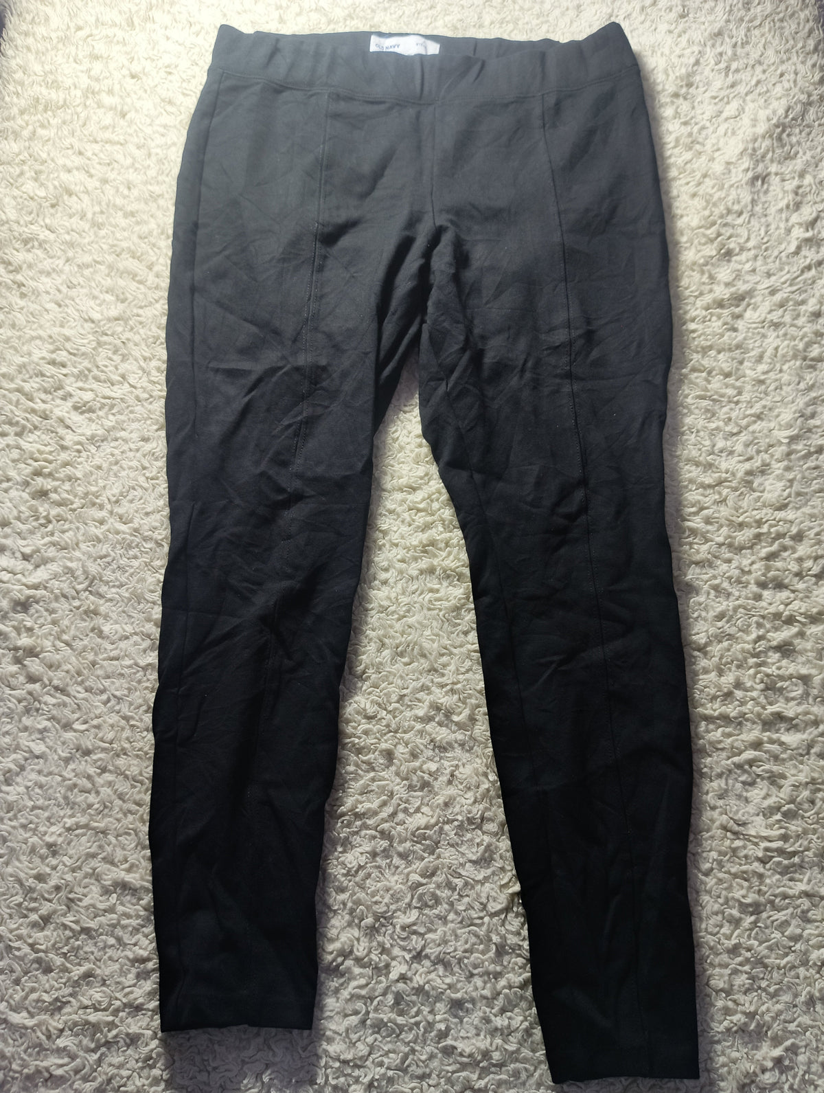 A pair of black wide-leg cropped pants laid flat on a textured beige carpet. The photo is taken from above, with a camera watermark at the bottom.