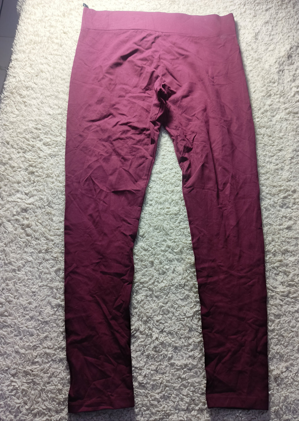 A pair of loose-fitting burgundy pants laid flat on a white textured carpet, photographed from above. The photo has a camera metadata overlay at the bottom.