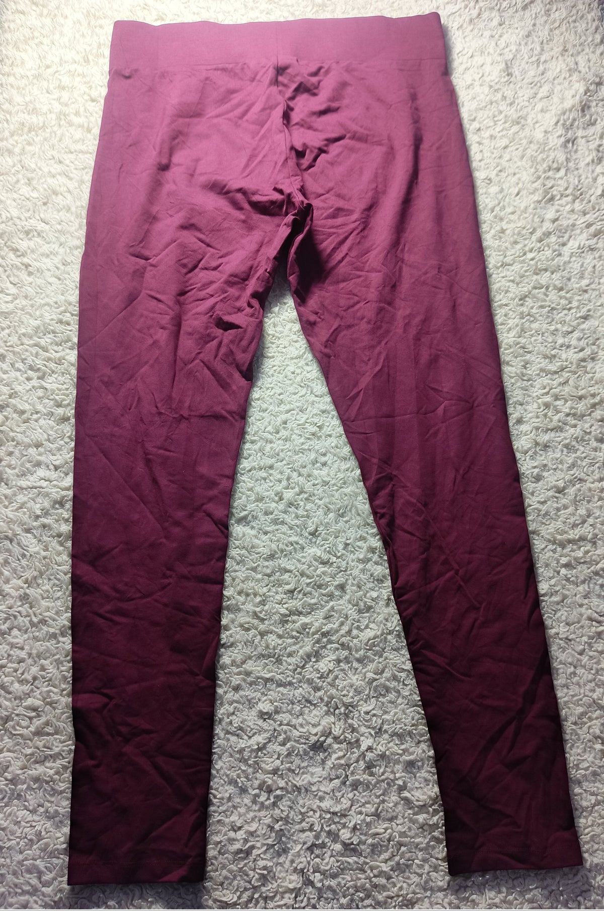 A pair of crinkled, deep magenta-purple leggings laid flat on a white shag rug. The image has a white border at the bottom with camera metadata text 'POVA 6 Neo' and '23mm f/1.