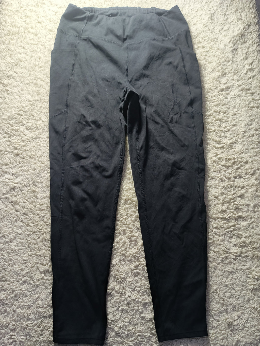 Black high-waisted leggings laid flat on a textured beige carpet, with a visible crotch opening.