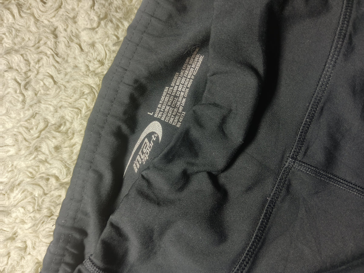 Close-up of a dark gray athletic jacket or hoodie laid flat on a textured cream rug, showing the inner lining, zipper, and printed care/information label.