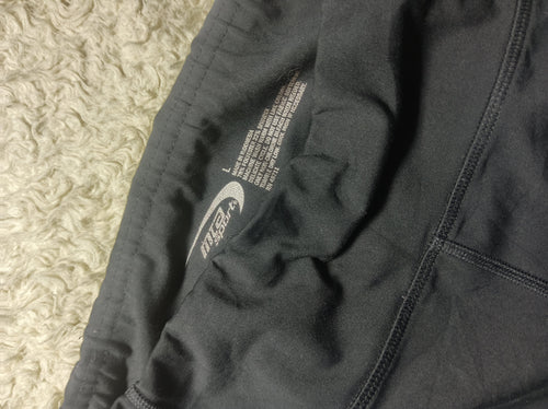 Close-up of a dark gray athletic jacket or hoodie laid flat on a textured cream rug, showing the inner lining, zipper, and printed care/information label.