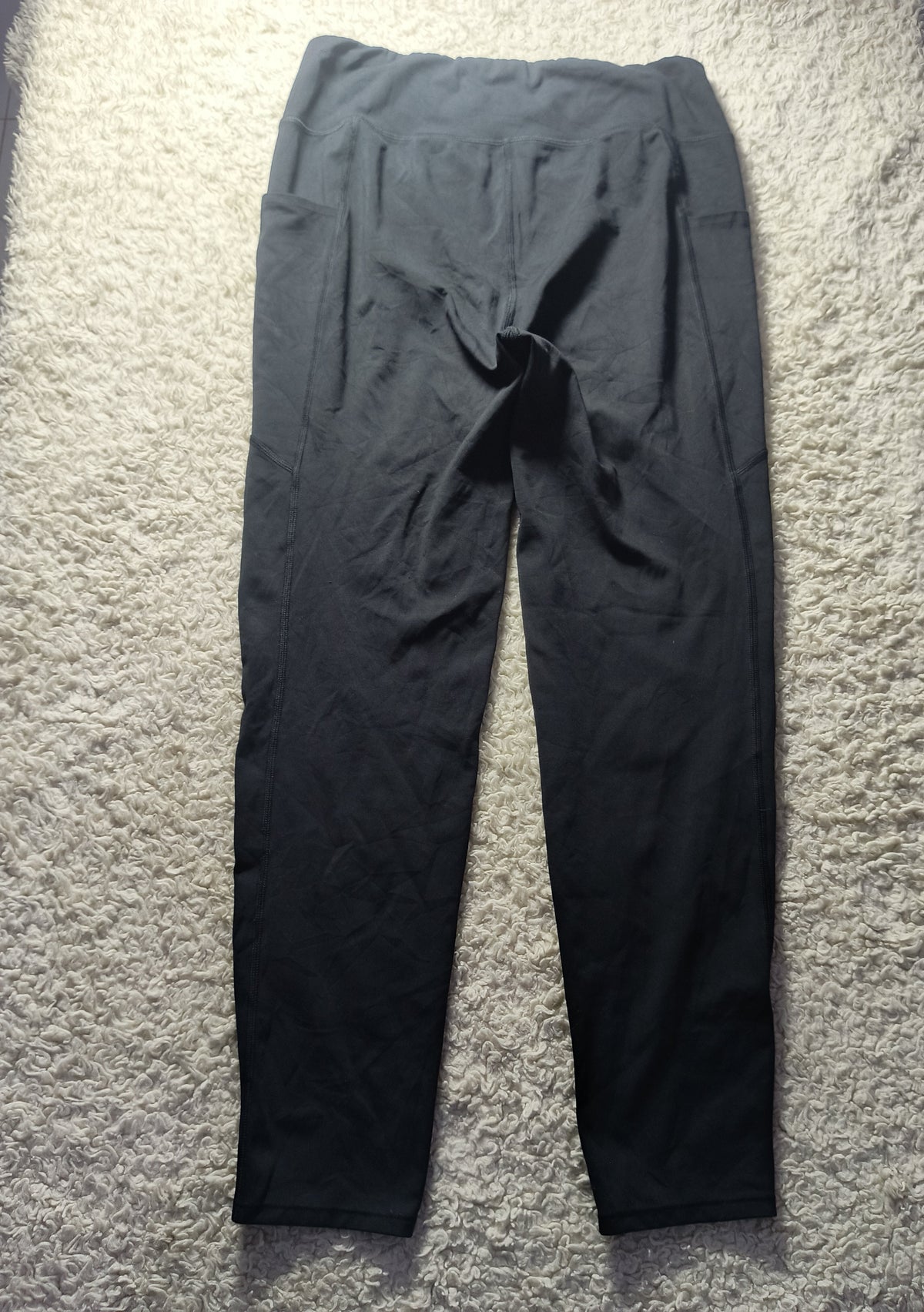 Black athletic leggings laid flat on a textured white carpet, with a small drawstring detail at the waist.