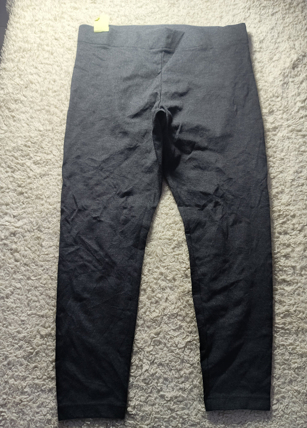 A pair of dark charcoal gray leggings laid flat on a textured gray carpet. The image has a camera watermark overlay at the bottom.