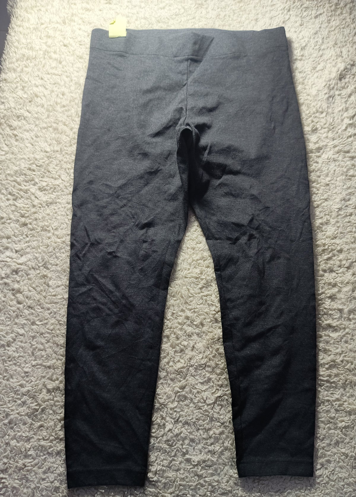 A pair of dark charcoal gray leggings laid flat on a textured gray carpet. The image has a camera watermark overlay at the bottom.
