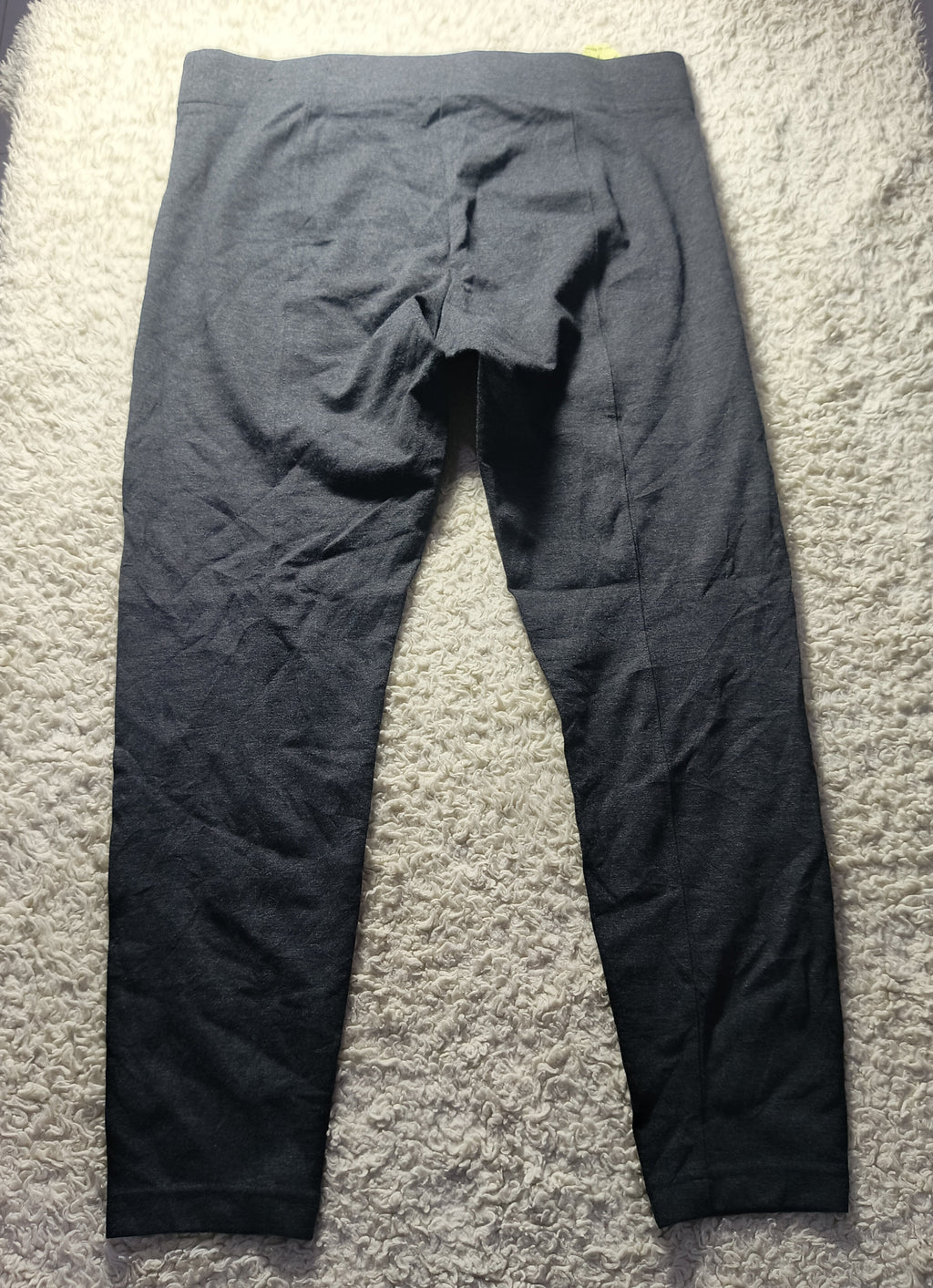 Dark gray athletic leggings laid flat on a white shag rug, showing the back view with a crotch opening and seam details.