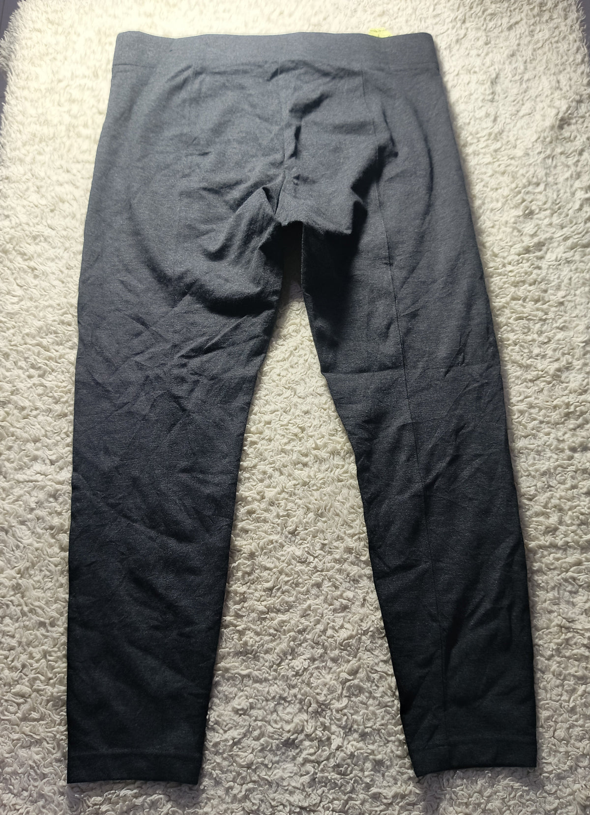 Dark gray athletic leggings laid flat on a white shag rug, showing the back view with a crotch opening and seam details.
