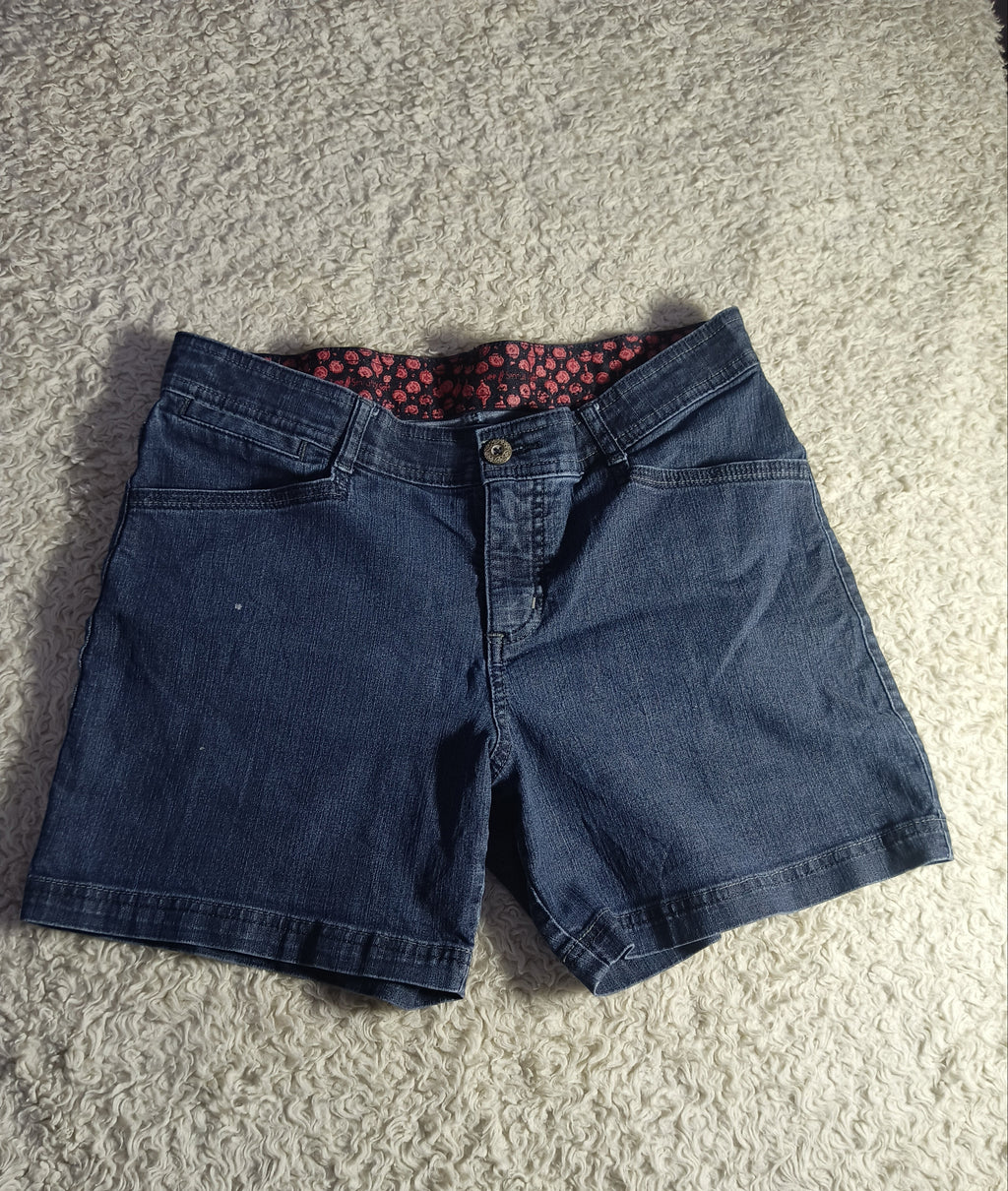 A pair of dark blue denim shorts laid flat on a textured beige carpet, showing a red and black patterned lining inside the waistband.