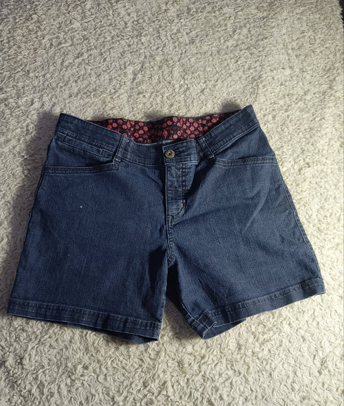 A pair of dark blue denim shorts laid flat on a textured beige carpet, showing a red and black patterned lining inside the waistband.