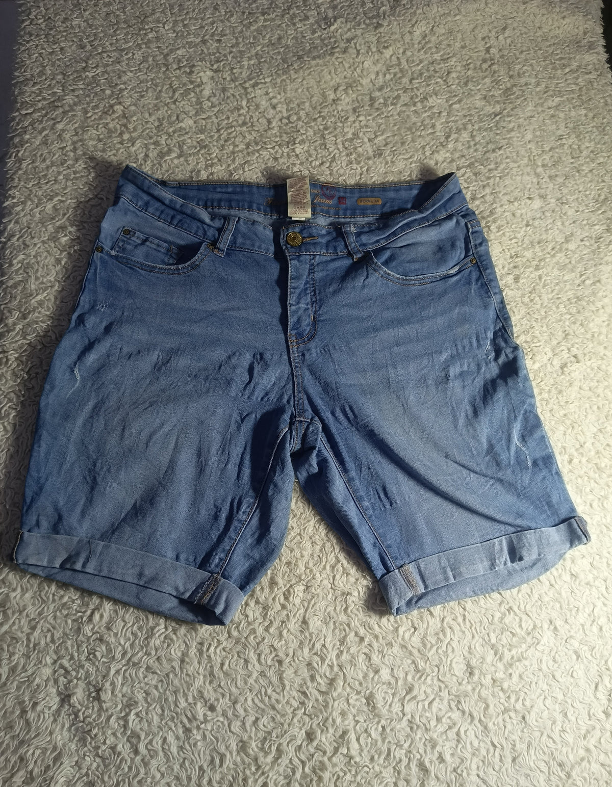 A pair of medium-wash blue denim shorts with rolled hems, laid flat on a textured gray carpet.