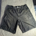 A pair of faded black denim shorts laid flat on a white shag rug.