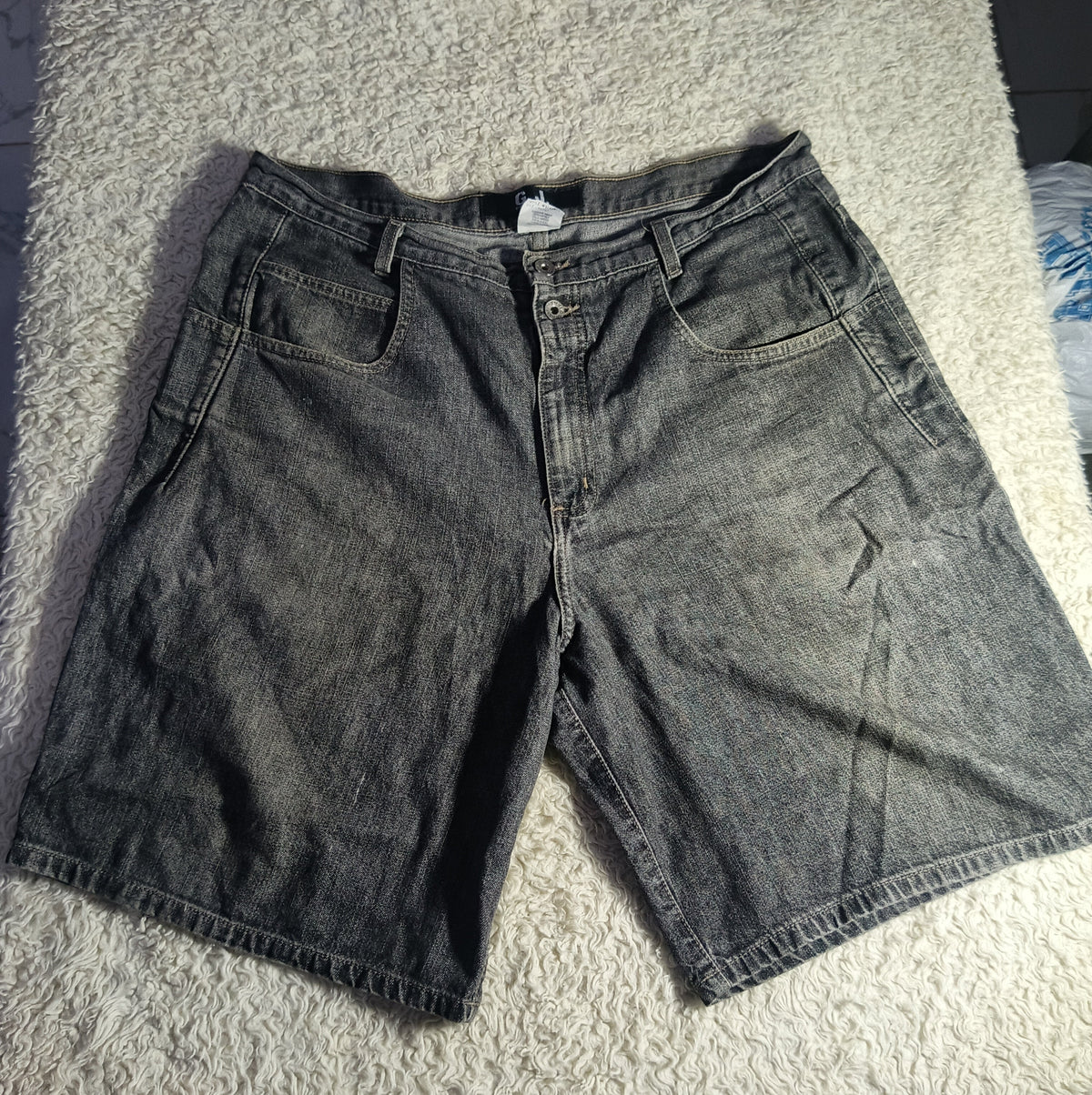 A pair of faded black denim shorts laid flat on a white shag rug.