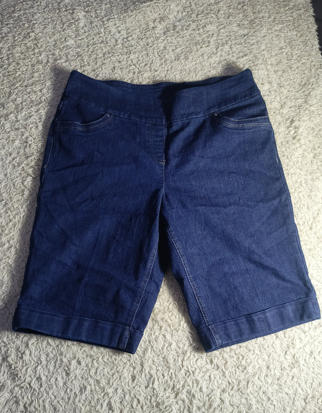 A pair of dark blue denim shorts laid flat on a textured gray carpet.