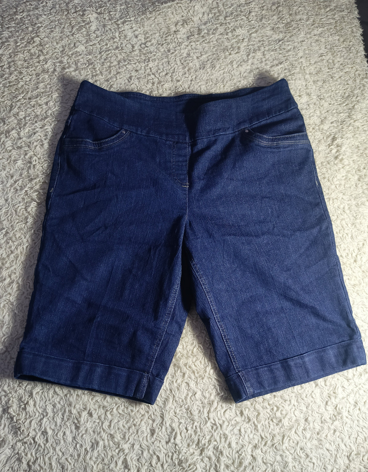 A pair of dark blue denim shorts laid flat on a textured gray carpet.