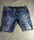 A pair of distressed blue denim shorts with frayed hems, laid flat on a textured gray carpet.