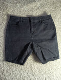 Dark charcoal gray denim shorts laid flat on a textured beige carpet. The photo is taken from above and includes a camera watermark at the bottom.